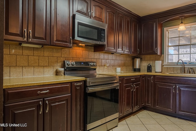 kitchen with light tile patterned floors, backsplash, dark brown cabinets, stainless steel appliances, and a sink