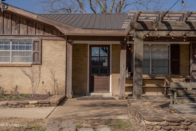 property entrance featuring a pergola, metal roof, and brick siding