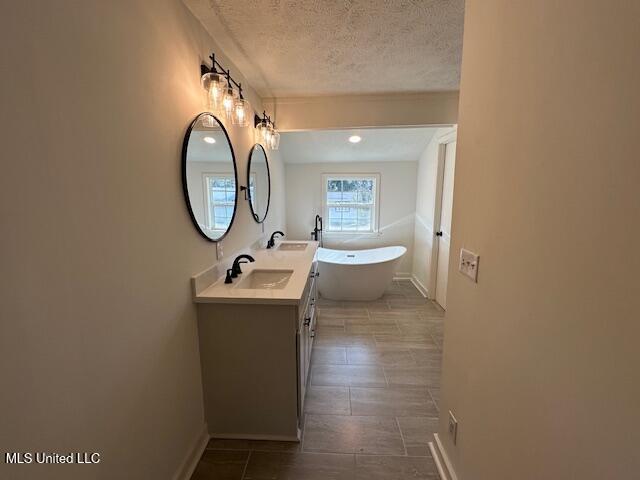 bathroom featuring vanity, a bath, and a textured ceiling