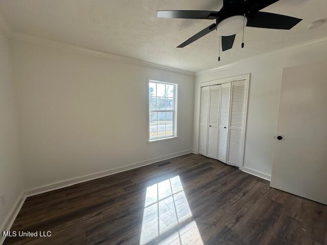 unfurnished bedroom with dark wood-type flooring, ceiling fan, crown molding, and a closet