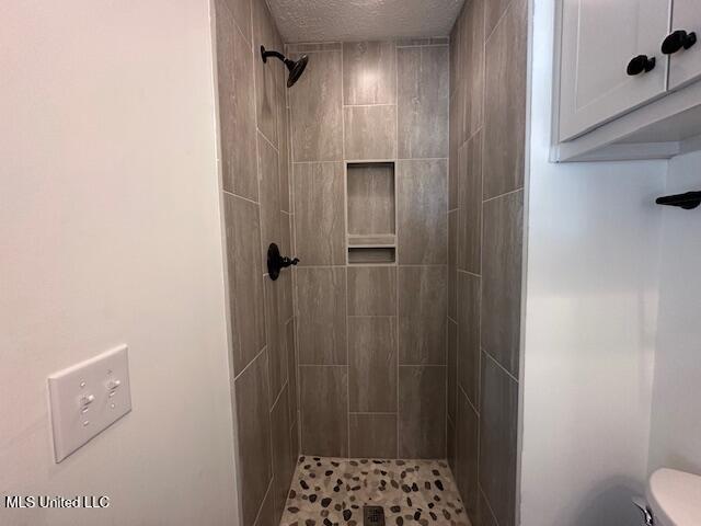 bathroom featuring a tile shower, a textured ceiling, and toilet