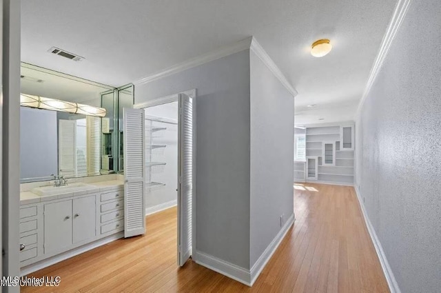 corridor featuring sink, ornamental molding, and light wood-type flooring