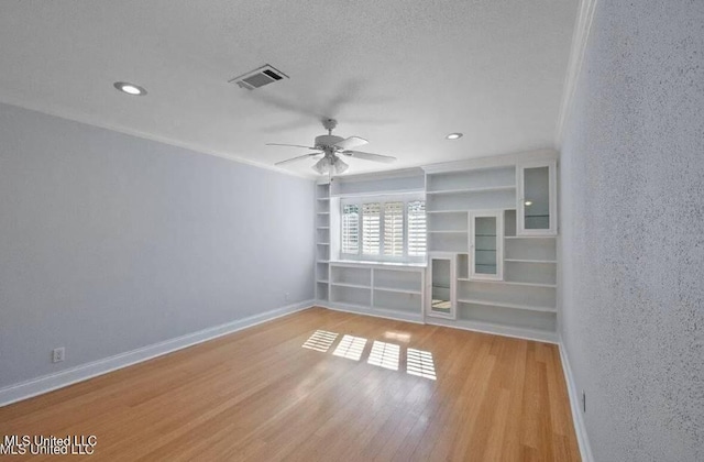 unfurnished living room featuring a textured ceiling, built in shelves, ornamental molding, light wood-type flooring, and ceiling fan