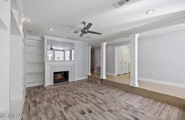 unfurnished living room featuring ornate columns, hardwood / wood-style flooring, a brick fireplace, ceiling fan, and ornamental molding