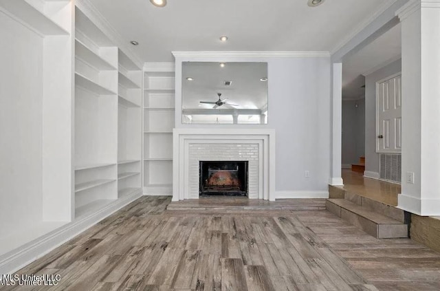 unfurnished living room featuring ceiling fan, a brick fireplace, wood-type flooring, built in features, and ornamental molding