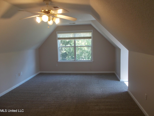 additional living space featuring dark carpet, lofted ceiling, a textured ceiling, and ceiling fan