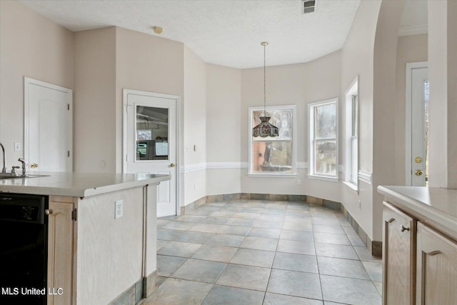 kitchen with black dishwasher, light tile patterned flooring, a textured ceiling, hanging light fixtures, and light brown cabinets