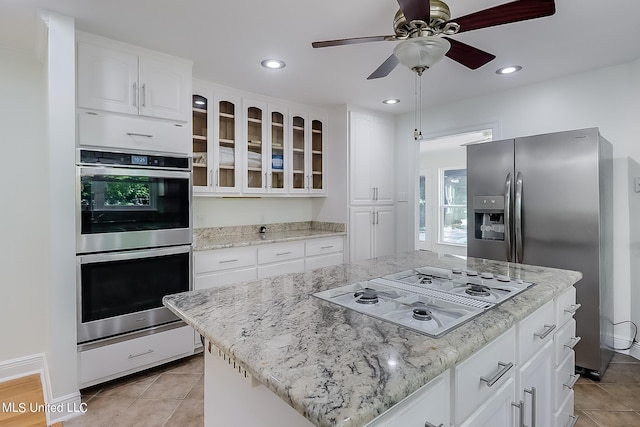 kitchen featuring ceiling fan, appliances with stainless steel finishes, white cabinetry, light stone counters, and a kitchen island