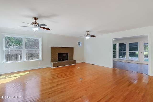 unfurnished living room with ceiling fan, a brick fireplace, and light hardwood / wood-style floors