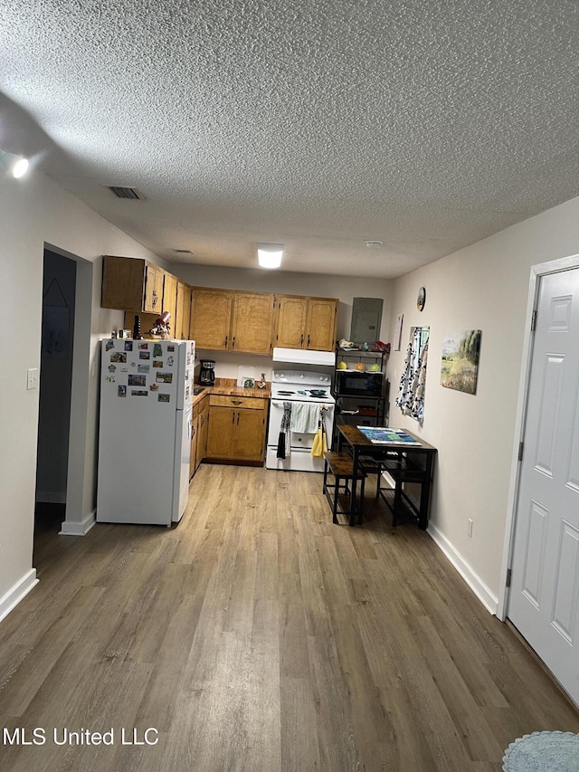 kitchen featuring white appliances, wood finished floors, a textured ceiling, visible vents, and under cabinet range hood