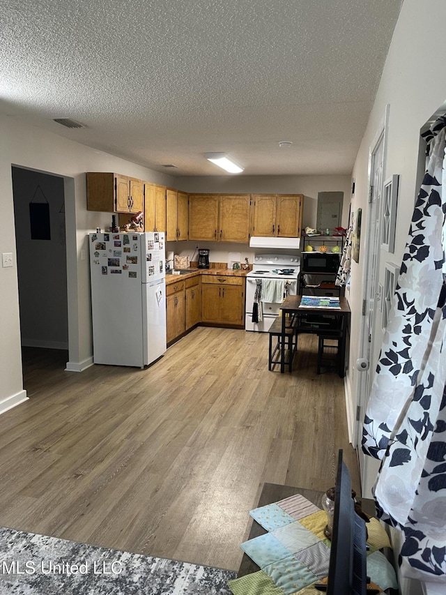 kitchen with brown cabinets, white appliances, a textured ceiling, and light wood-style floors