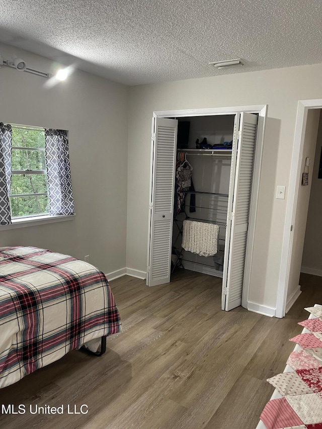 bedroom with baseboards, a closet, a textured ceiling, and wood finished floors