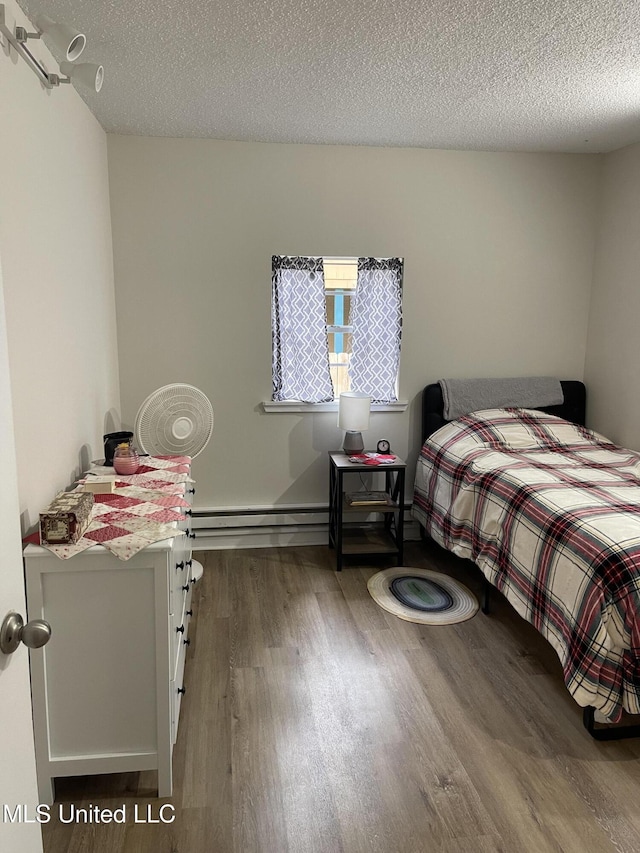 bedroom featuring a baseboard heating unit, a textured ceiling, and wood finished floors