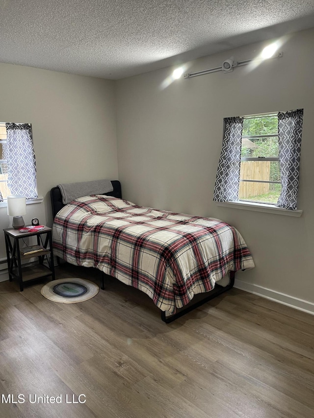 bedroom featuring a textured ceiling, baseboards, and wood finished floors