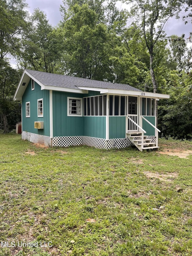 ranch-style home with entry steps, a front lawn, board and batten siding, a sunroom, and a shingled roof