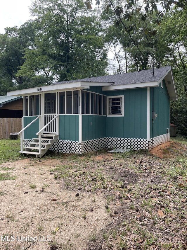 rear view of property featuring entry steps, a sunroom, and roof with shingles