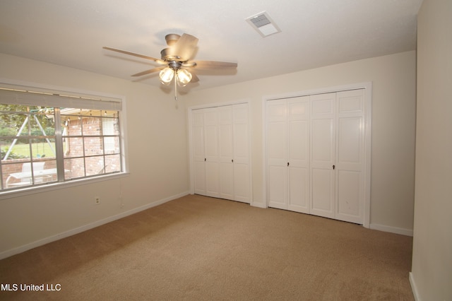 unfurnished bedroom with ceiling fan, light colored carpet, and multiple closets