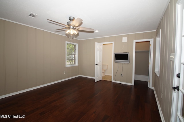 unfurnished bedroom featuring a closet, a walk in closet, ornamental molding, dark wood-type flooring, and ceiling fan