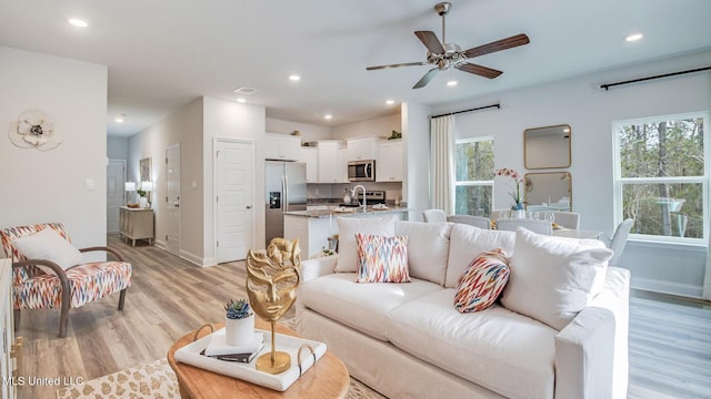 living area with healthy amount of natural light, light wood finished floors, ceiling fan, baseboards, and recessed lighting