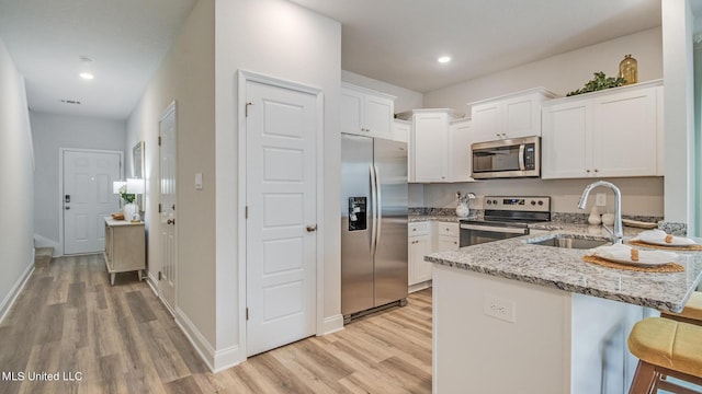 kitchen featuring appliances with stainless steel finishes, a sink, a peninsula, light wood finished floors, and recessed lighting
