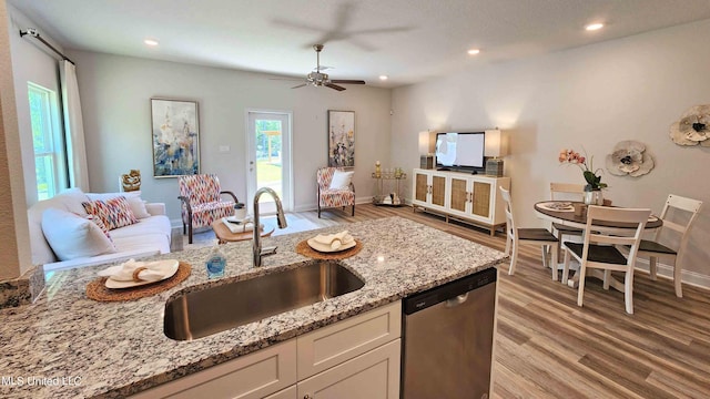 kitchen with dishwasher, a sink, light wood-type flooring, light stone countertops, and open floor plan
