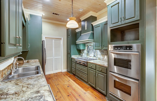 kitchen featuring appliances with stainless steel finishes, light wood-type flooring, wall chimney range hood, sink, and hanging light fixtures