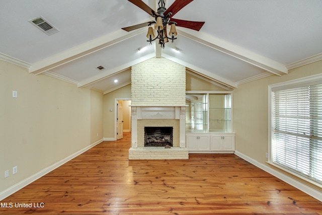 unfurnished living room with ceiling fan, a brick fireplace, lofted ceiling with beams, crown molding, and light hardwood / wood-style floors