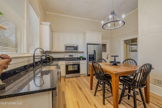 kitchen with white cabinetry, hanging light fixtures, a chandelier, appliances with stainless steel finishes, and light wood-type flooring