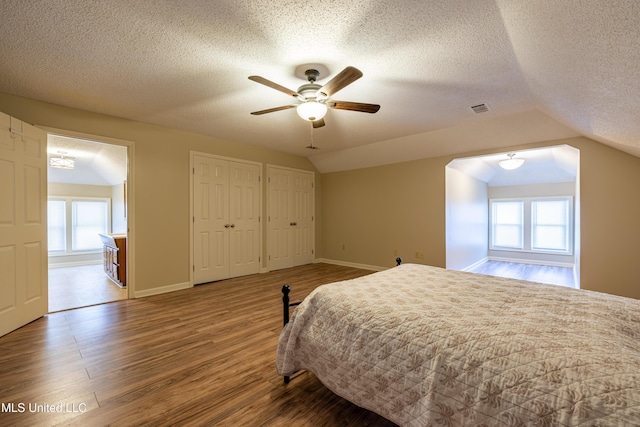 bedroom with a textured ceiling, two closets, vaulted ceiling, and hardwood / wood-style flooring