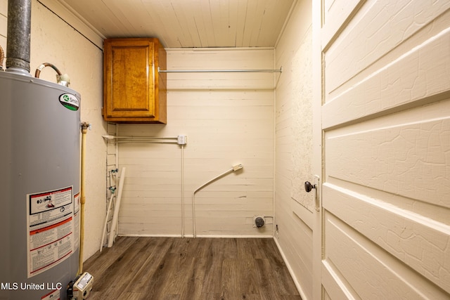 clothes washing area with dark hardwood / wood-style floors, cabinets, wooden walls, and water heater