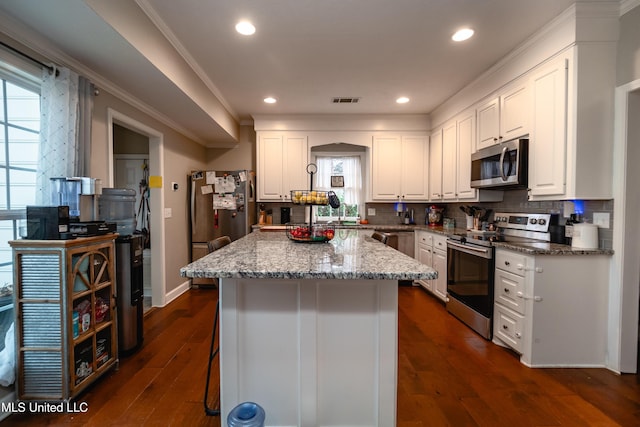 kitchen with white cabinetry, stainless steel appliances, a kitchen island, and light stone counters