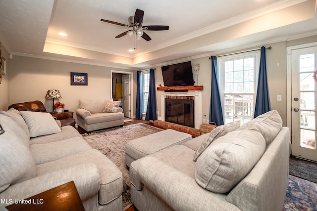 living room featuring a fireplace, ornamental molding, a raised ceiling, and ceiling fan