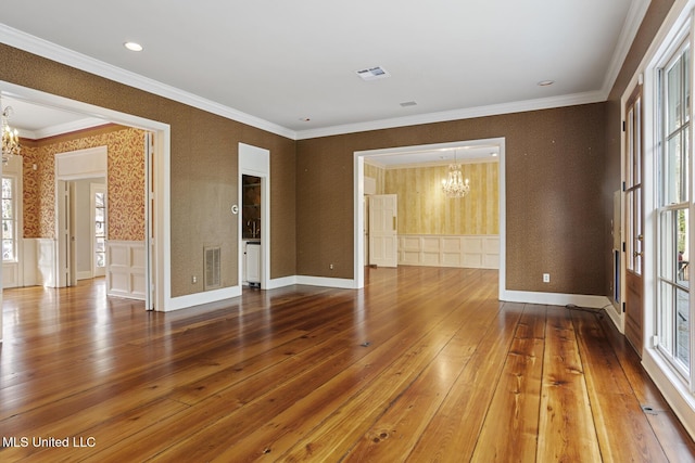 spare room featuring a notable chandelier, ornamental molding, hardwood / wood-style floors, and a healthy amount of sunlight