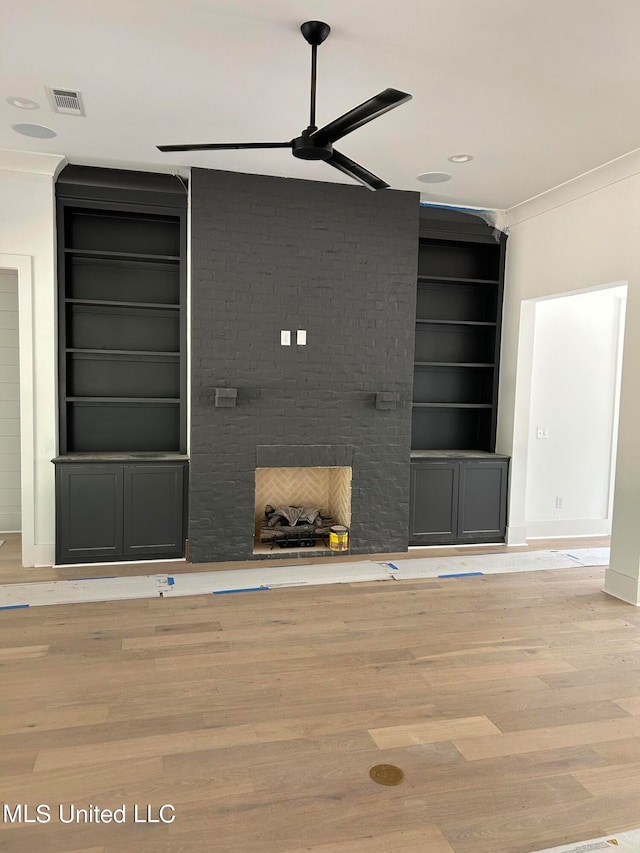 unfurnished living room with built in shelves, light wood-type flooring, crown molding, and a brick fireplace