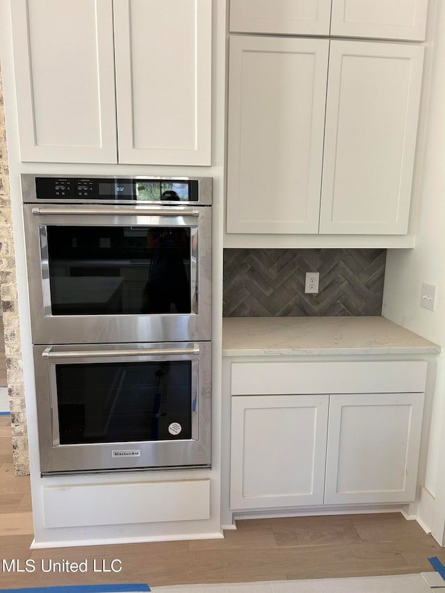 kitchen with tasteful backsplash, light stone countertops, white cabinets, and stainless steel double oven