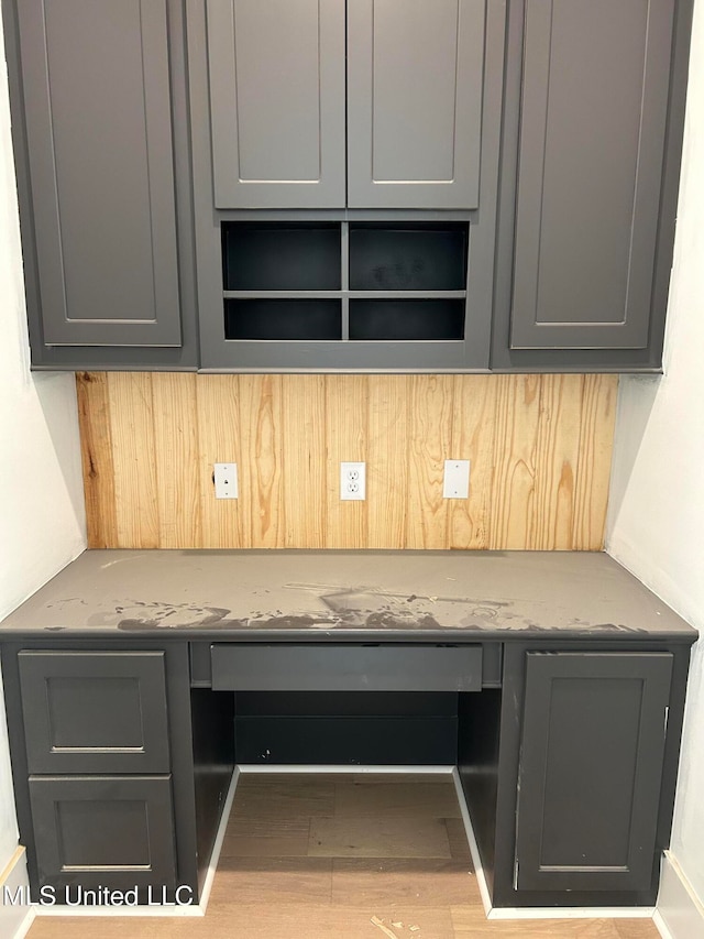 kitchen with gray cabinetry, light stone counters, built in desk, and light wood-type flooring