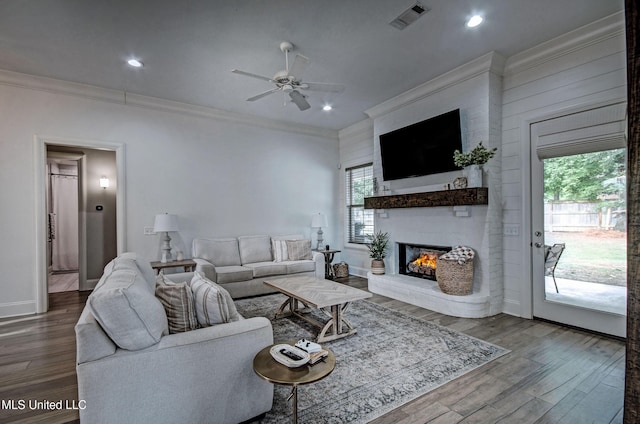 living area featuring ornamental molding, plenty of natural light, a ceiling fan, a brick fireplace, and wood finished floors