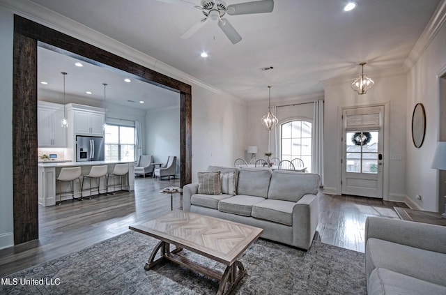 living room featuring plenty of natural light, a chandelier, wood finished floors, ornamental molding, and a ceiling fan