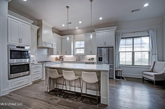 kitchen with stainless steel appliances, a kitchen island, light countertops, custom exhaust hood, and a sink