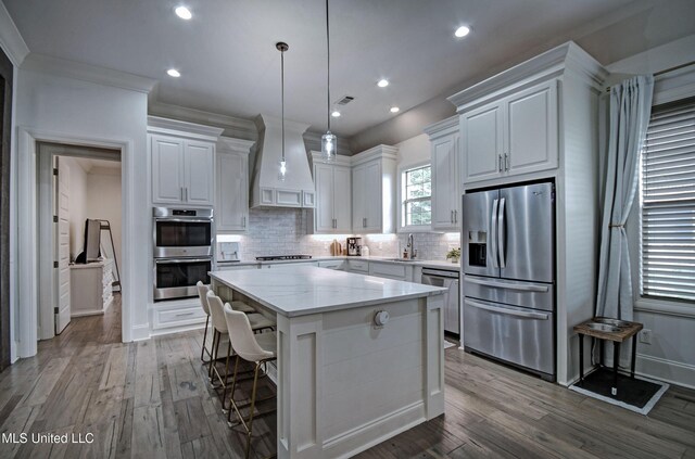 kitchen featuring appliances with stainless steel finishes, a sink, white cabinetry, premium range hood, and wood-type flooring