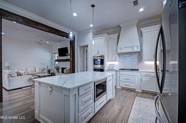 kitchen featuring appliances with stainless steel finishes, premium range hood, crown molding, white cabinetry, and backsplash