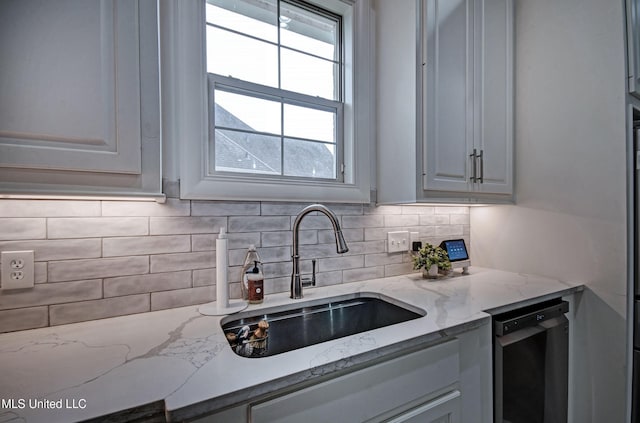 kitchen with a sink, dishwasher, backsplash, and light stone counters