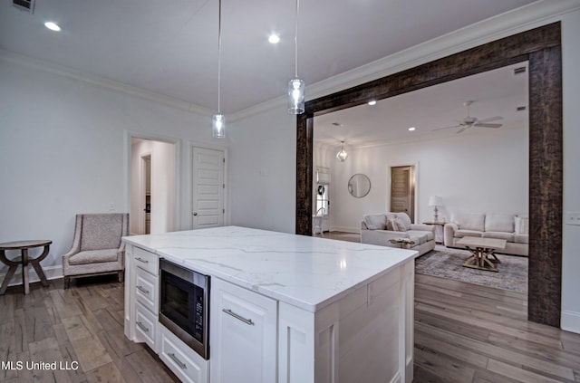 kitchen with stainless steel microwave, ornamental molding, white cabinets, dark wood finished floors, and light stone counters
