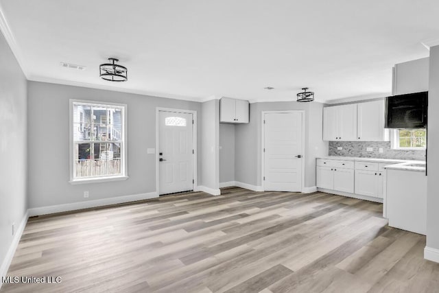 interior space with baseboards, white cabinetry, crown molding, visible vents, and light wood finished floors
