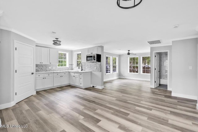 kitchen featuring stainless steel microwave, tasteful backsplash, light wood-type flooring, light countertops, and crown molding