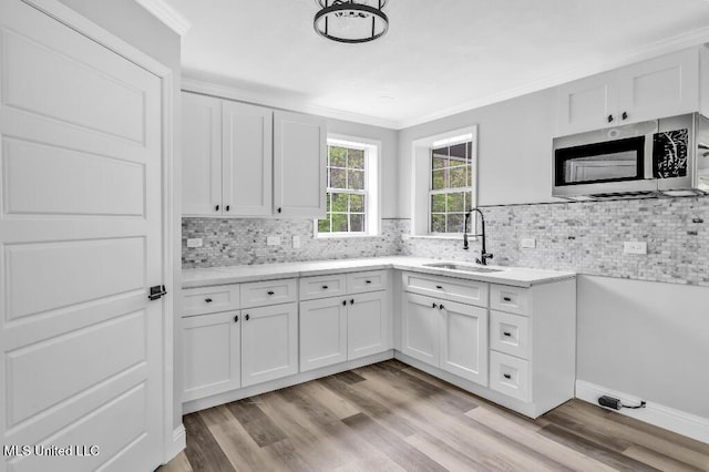 kitchen with white cabinets, a sink, crown molding, stainless steel microwave, and decorative backsplash