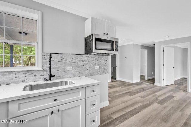 kitchen featuring a sink, crown molding, stainless steel microwave, white cabinetry, and decorative backsplash