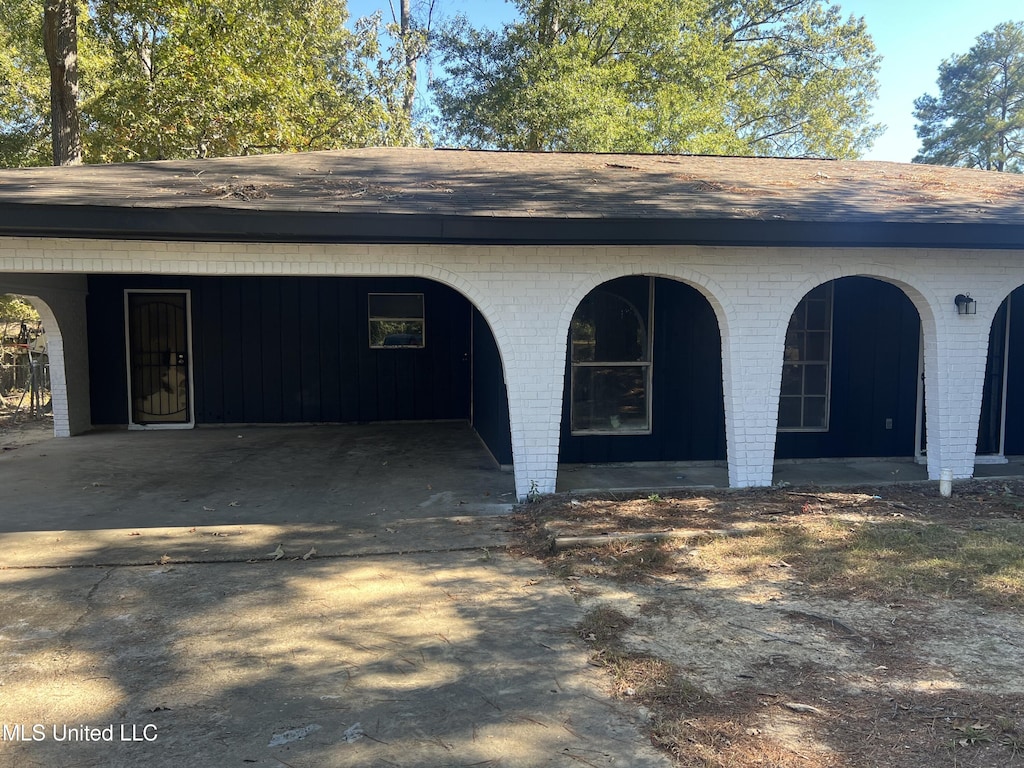 exterior space featuring a shingled roof, an attached carport, and brick siding