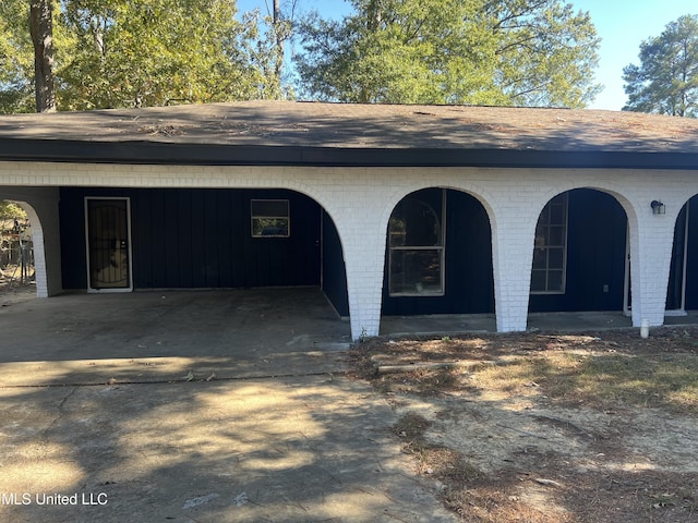 exterior space featuring a shingled roof, an attached carport, and brick siding