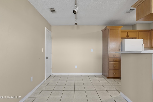 kitchen with light tile patterned floors, visible vents, freestanding refrigerator, and a textured ceiling